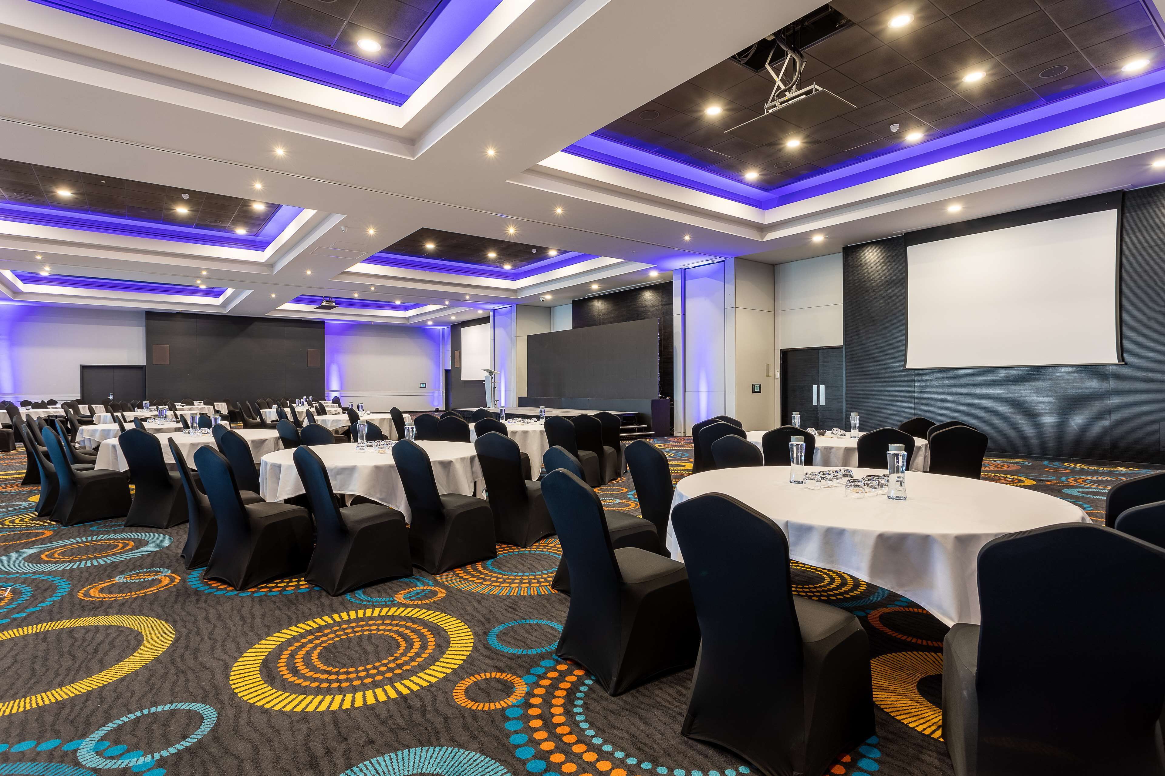 A conference room with round tables, black chairs, and a carpet with circular patterns.