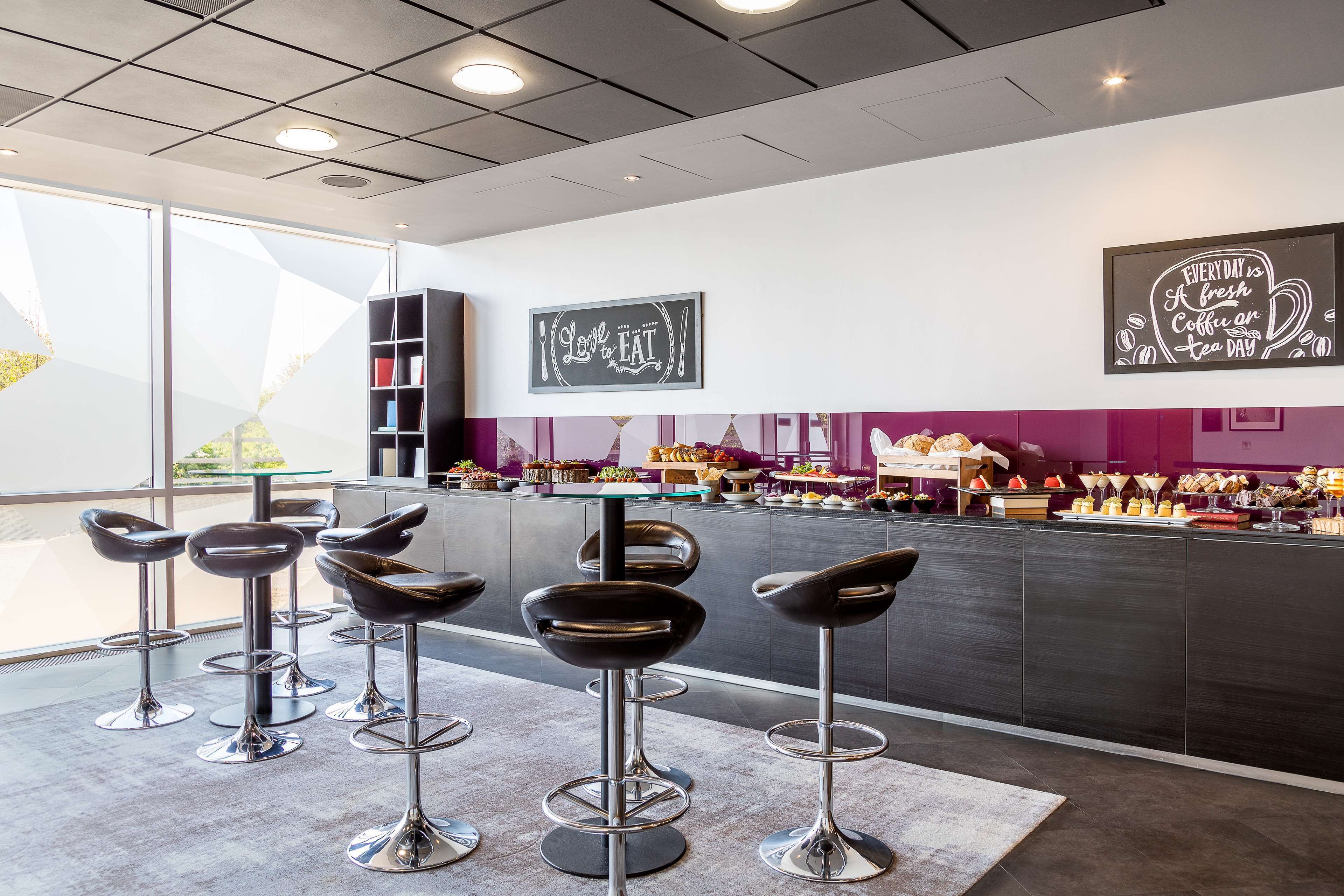 Een moderne bar met barkrukken, een toonbank met eten en drinken, en inspirerende muurkunst.