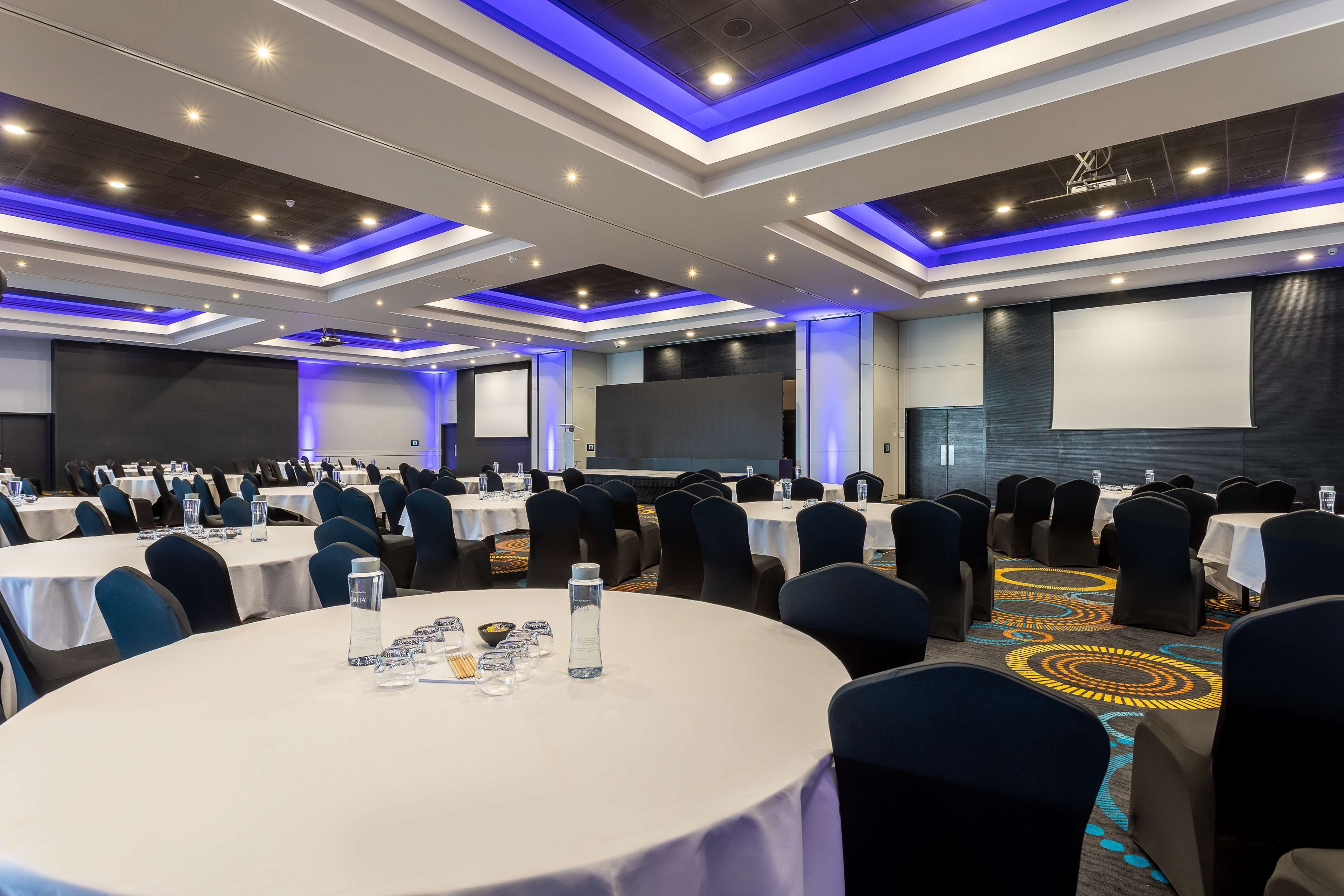 A conference room with round tables, chairs, and a projector screen.