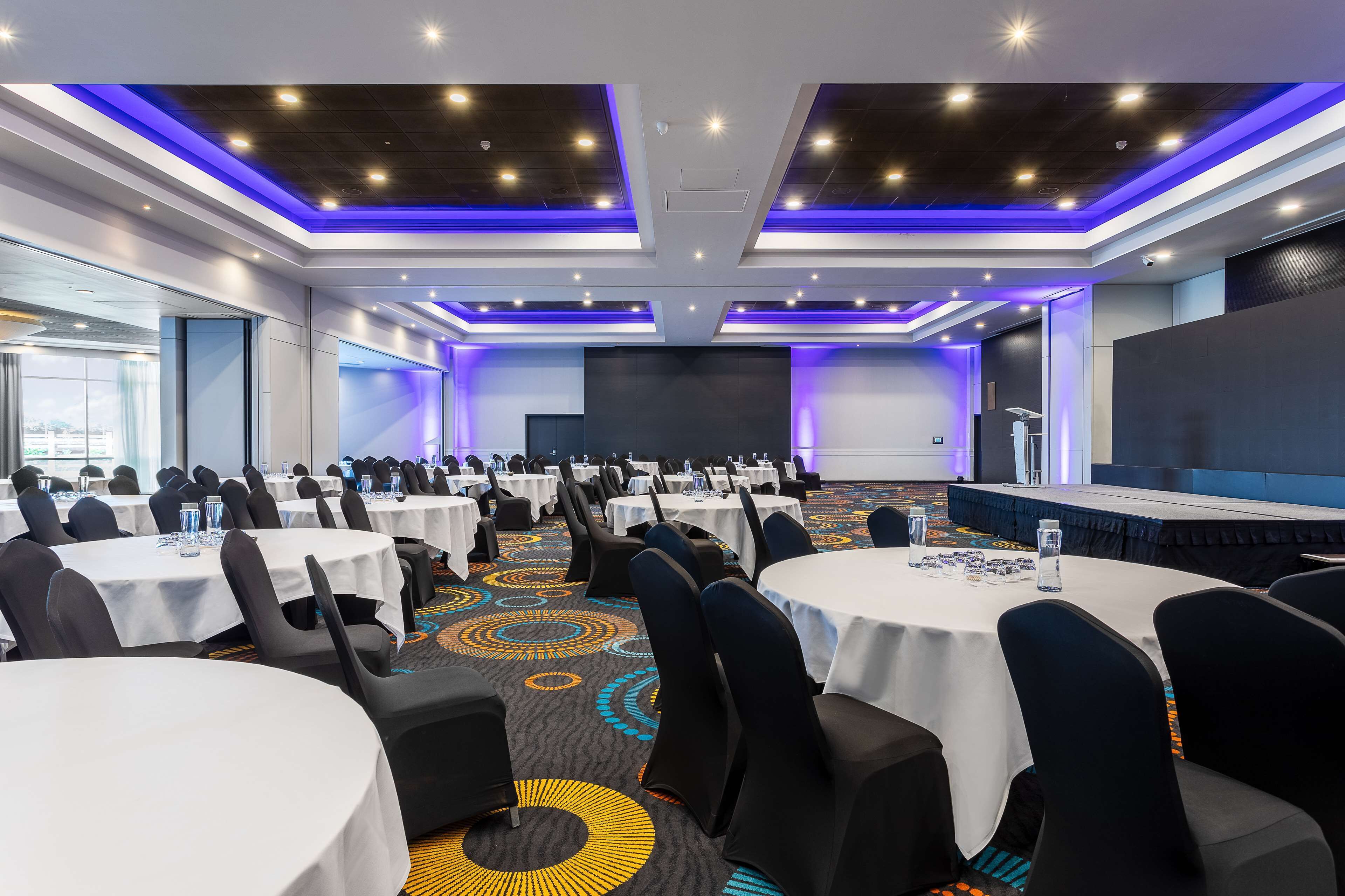A conference room with round tables, black chairs, and a stage.