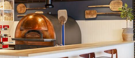 A kitchen with a wood-fired oven, a blue spatula, and a plant on the counter.