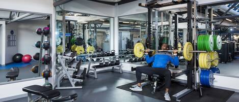 A gym with weightlifting equipment, benches, and mirrors.