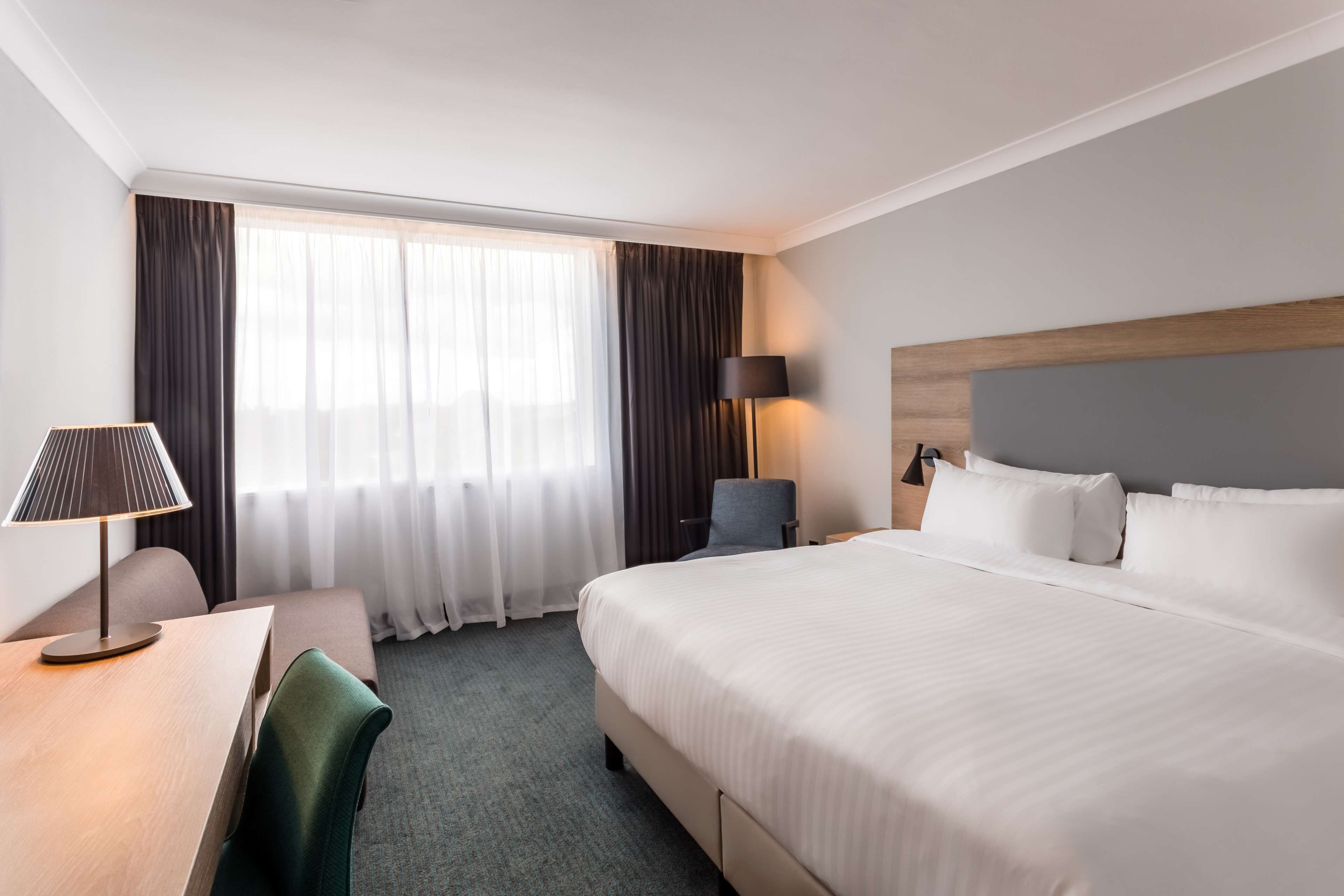 Una habitación de hotel con una cama grande, un escritorio con lámpara, una silla y una ventana con cortinas.