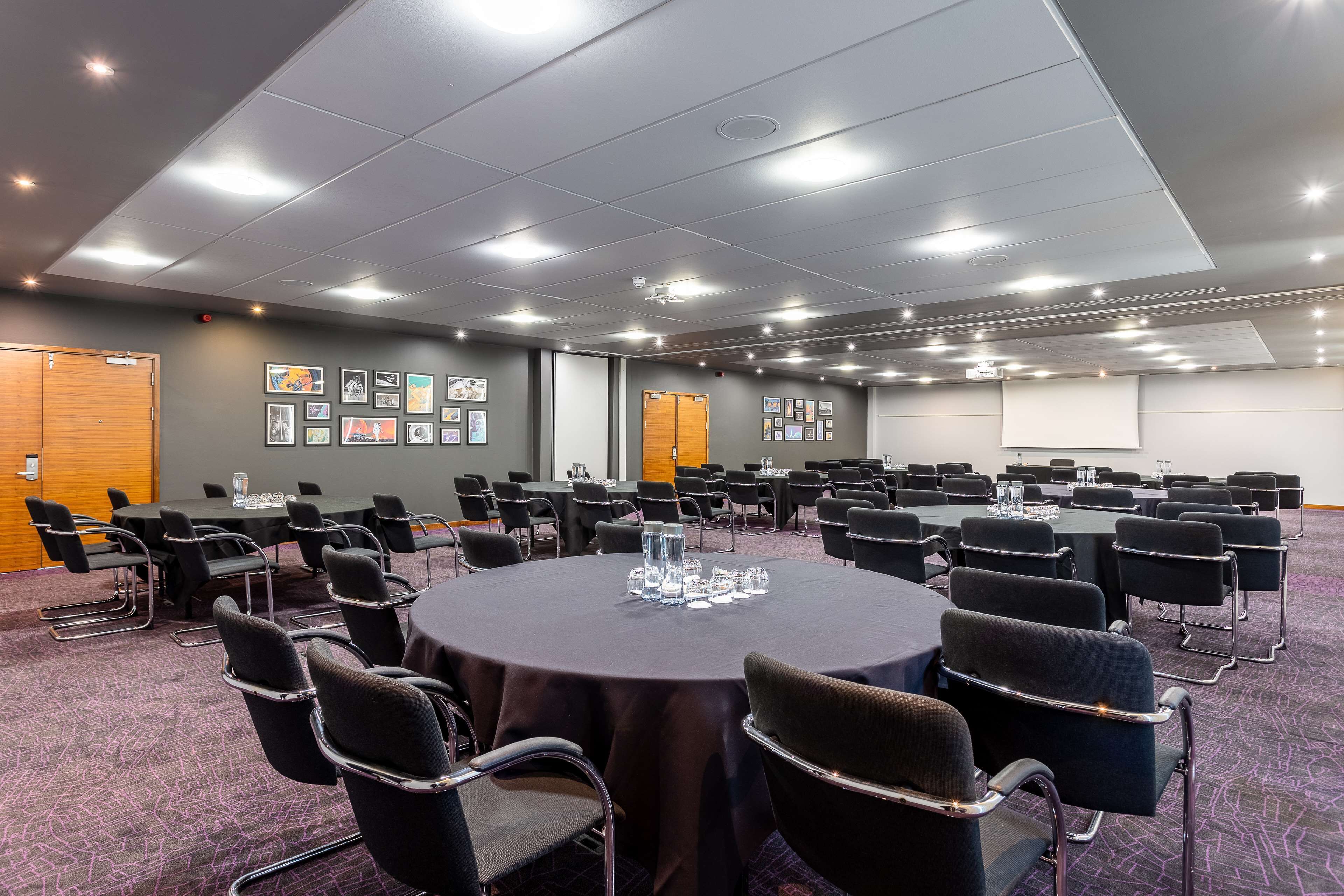 A conference room with round tables, black chairs, and framed pictures on the walls.