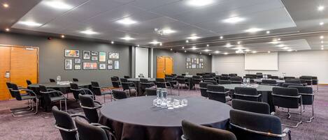 A conference room with round tables, black chairs, and framed pictures on the walls.
