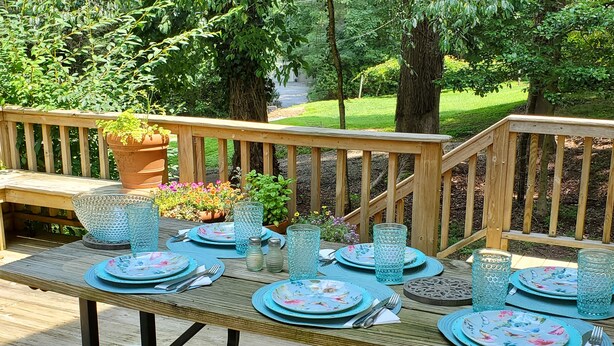 A wooden deck with a table set for four, surrounded by greenery and trees. - 1920's and 2020's...the best of both! (Saluda)