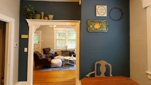 A room with a dark blue wall, a wooden dining table, and a cozy seating area with a sofa and ottomans. - 1920's and 2020's...the best of both! (Saluda)