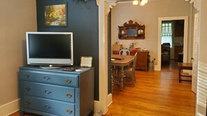 A room with a television on a dresser, a wooden dining table, and a kitchen in the background. - 1920's and 2020's...the best of both! (Saluda)