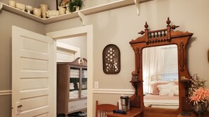 A bedroom with a wooden dresser, a vanity with a mirror, a shelf with decorative items, and a closet with folded towels. - 1920's and 2020's...the best of both! (Saluda)