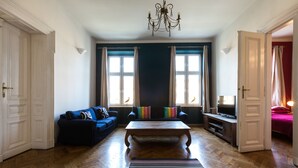 A spacious living room with a wooden coffee table, a blue sofa, and a television on a wooden stand.