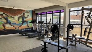 Una palestra con attrezzature cardio, pesi e un murale raffigurante dei corridori.