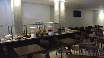 Una barra de desayuno con diferentes alimentos y bebidas, rodeada de mesas y sillas.