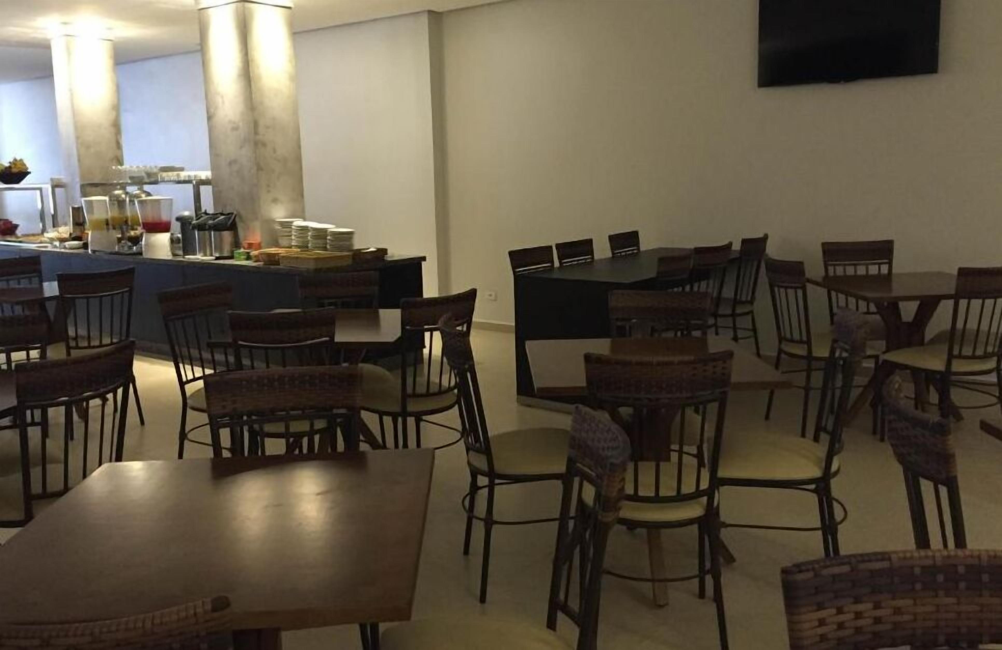 A dining area with multiple tables and chairs, a buffet counter with food and beverages, and a flat-screen TV mounted on the wall.
