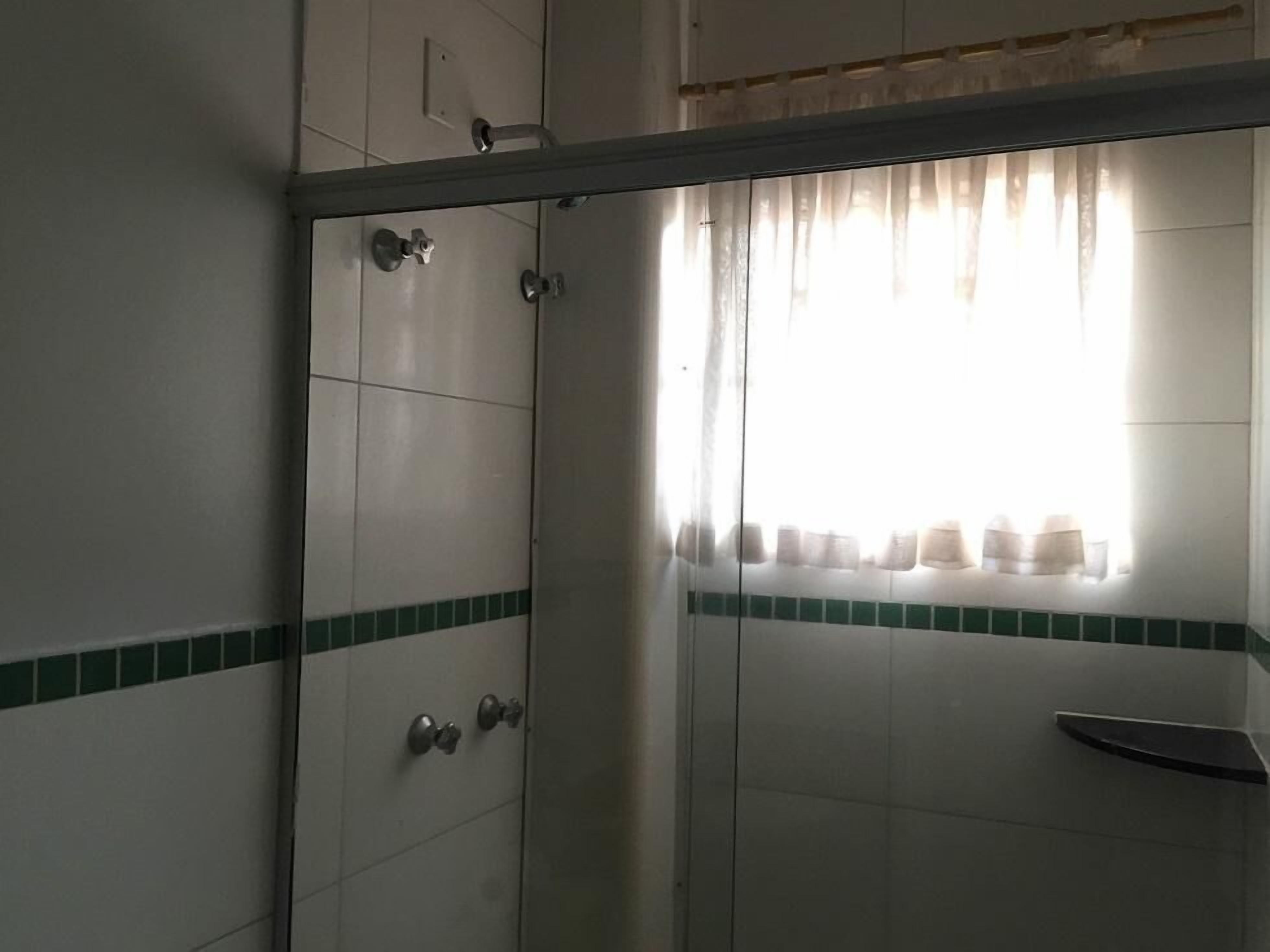 Baño con ducha, paredes de azulejos y una ventana con cortinas.