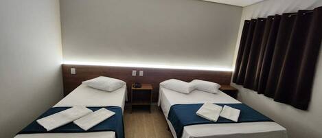 Ein Hotelzimmer mit zwei Einzelbetten, einem Nachttisch, einem kleinen Tisch und einem Fenster mit Vorhängen.