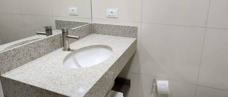 A modern bathroom with a granite countertop sink, a toilet, and a towel rack.