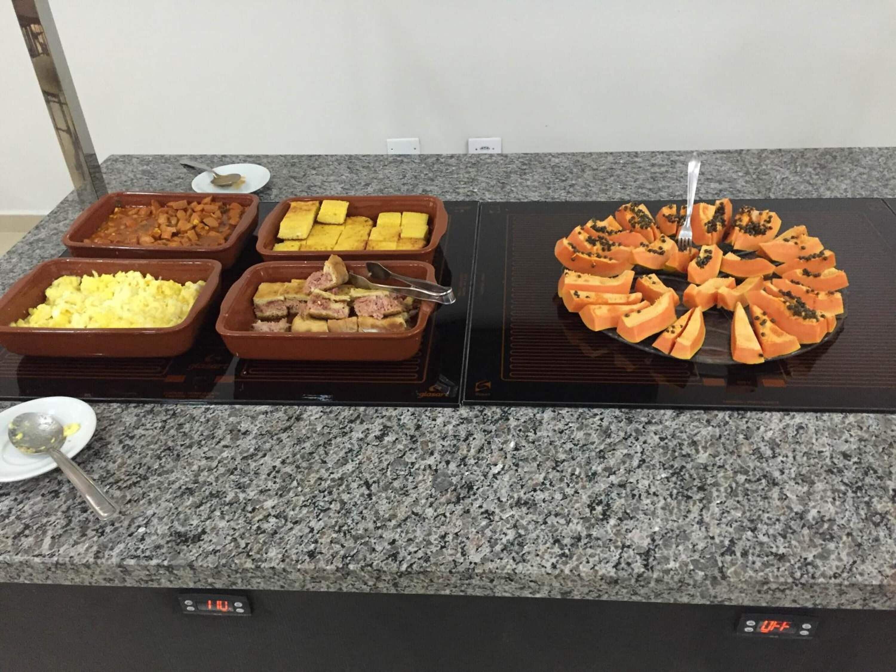 A buffet table with various dishes including scrambled eggs, meat, and sliced vegetables.