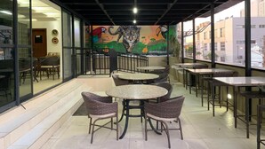 Patio esterno con tavoli rotondi e sedie in vimini, un murale raffigurante animali selvatici e vista su edifici attraverso ampie vetrate.