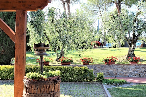 Eine hölzerne Pergola mit einem rustikalen Vogelhaus, umgeben von einer Steinmauer und Kübeln mit roten Blumen.