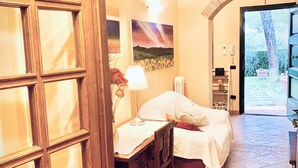 Ein Schlafzimmer mit Bett, Schreibtisch und Stuhl. An der Wand hängt ein Bild und das Fenster bietet einen Blick ins Freie.