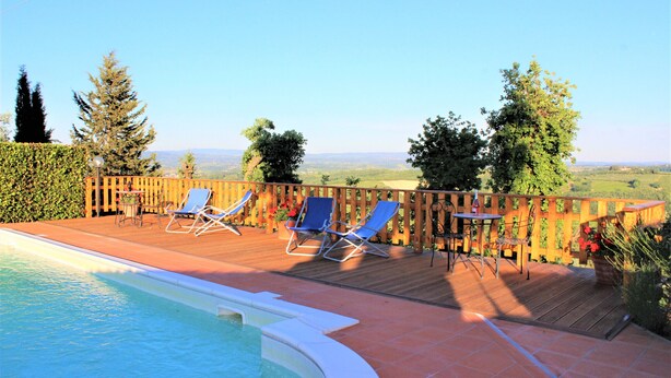 Ein Poolbereich mit Holzterrasse, Liegestühlen und Blick ins Grüne.
