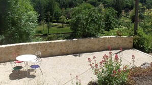 A patio with a stone wall, a round table, and metal chairs.