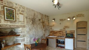 A rustic kitchen with stone walls, wooden furniture, a dining table, and a small sink.