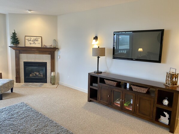 A living room with a fireplace, a TV mounted on the wall, a lamp, and a wooden entertainment center.