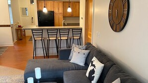 Un salon moderne avec un canapé d’angle gris, une table basse en bois et une grande horloge murale.