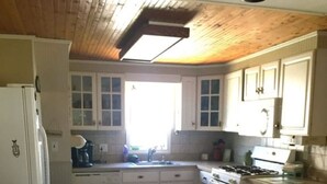 A kitchen with wooden ceiling, white cabinets, a central island, and a refrigerator.