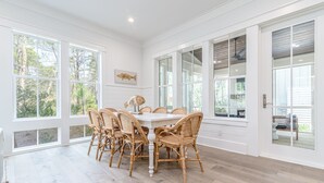 A spacious dining area with a white table and wicker chairs, large windows with a view of trees, and a ceiling fan. - Southern Sand: beach house with beautiful forest views (Santa Rosa Beach)