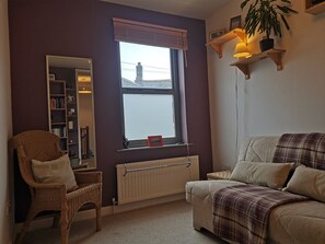 Un salon chaleureux avec une grande fenêtre, un fauteuil en osier, un canapé et une bibliothèque.