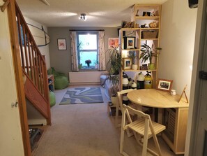 Un salon chaleureux avec un escalier en bois, un coin repas avec une table ronde et des chaises, et une bibliothèque remplie de divers objets.