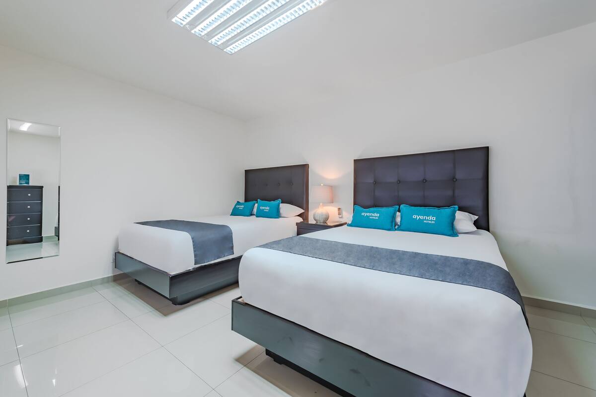A hotel room with two beds, a large mirror, and a modern ceiling light fixture.