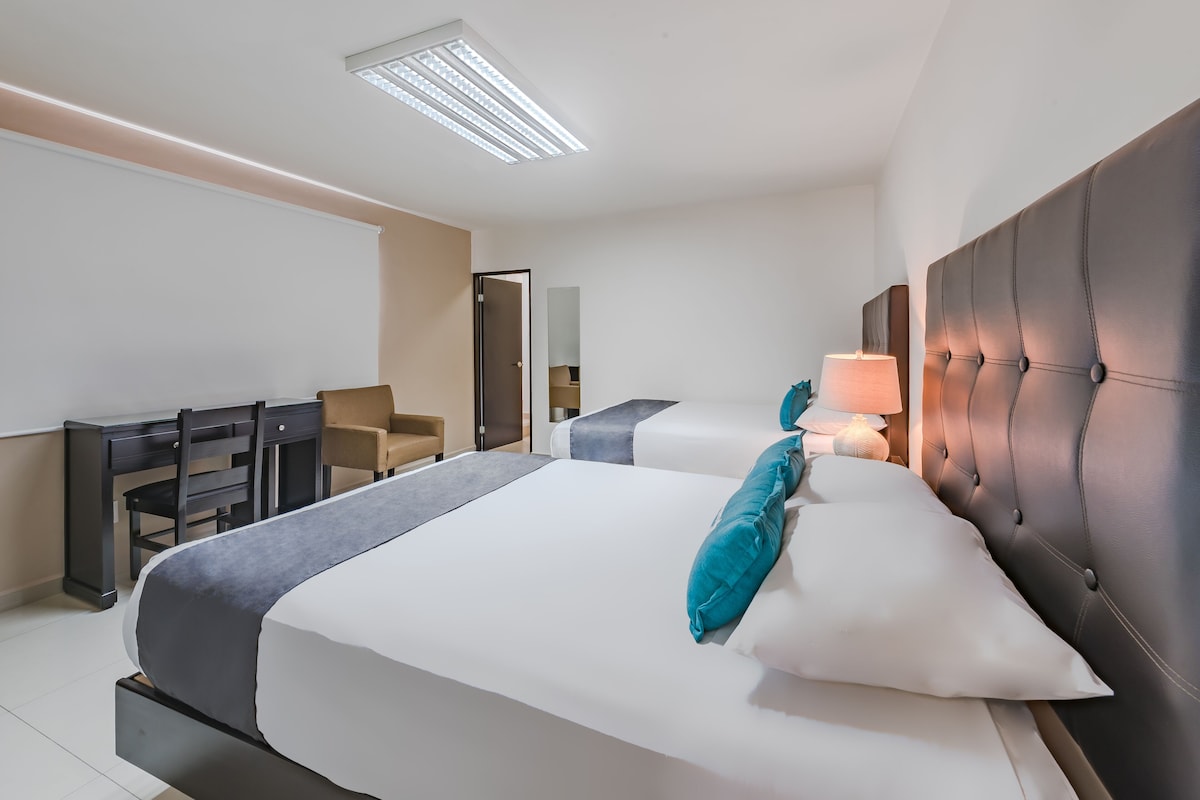 A hotel room with two beds, a desk, and a chair.