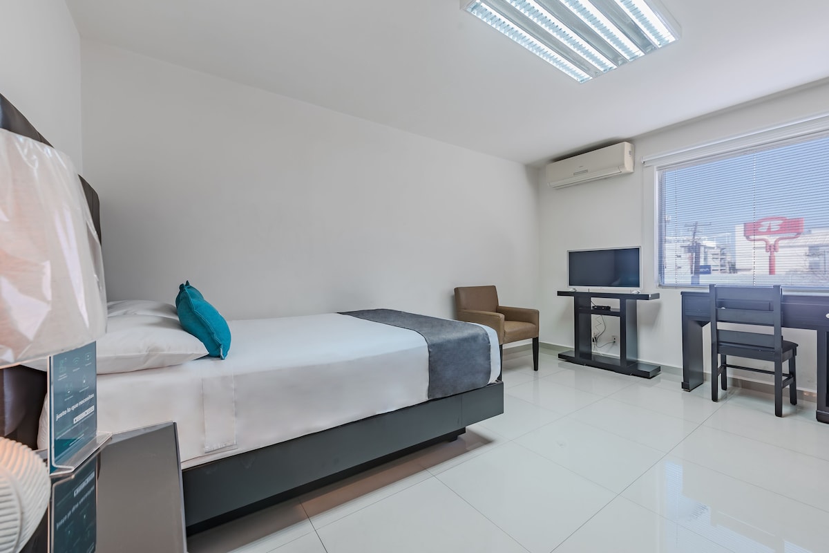 A modern hotel room with a bed, a desk, a chair, and a TV.