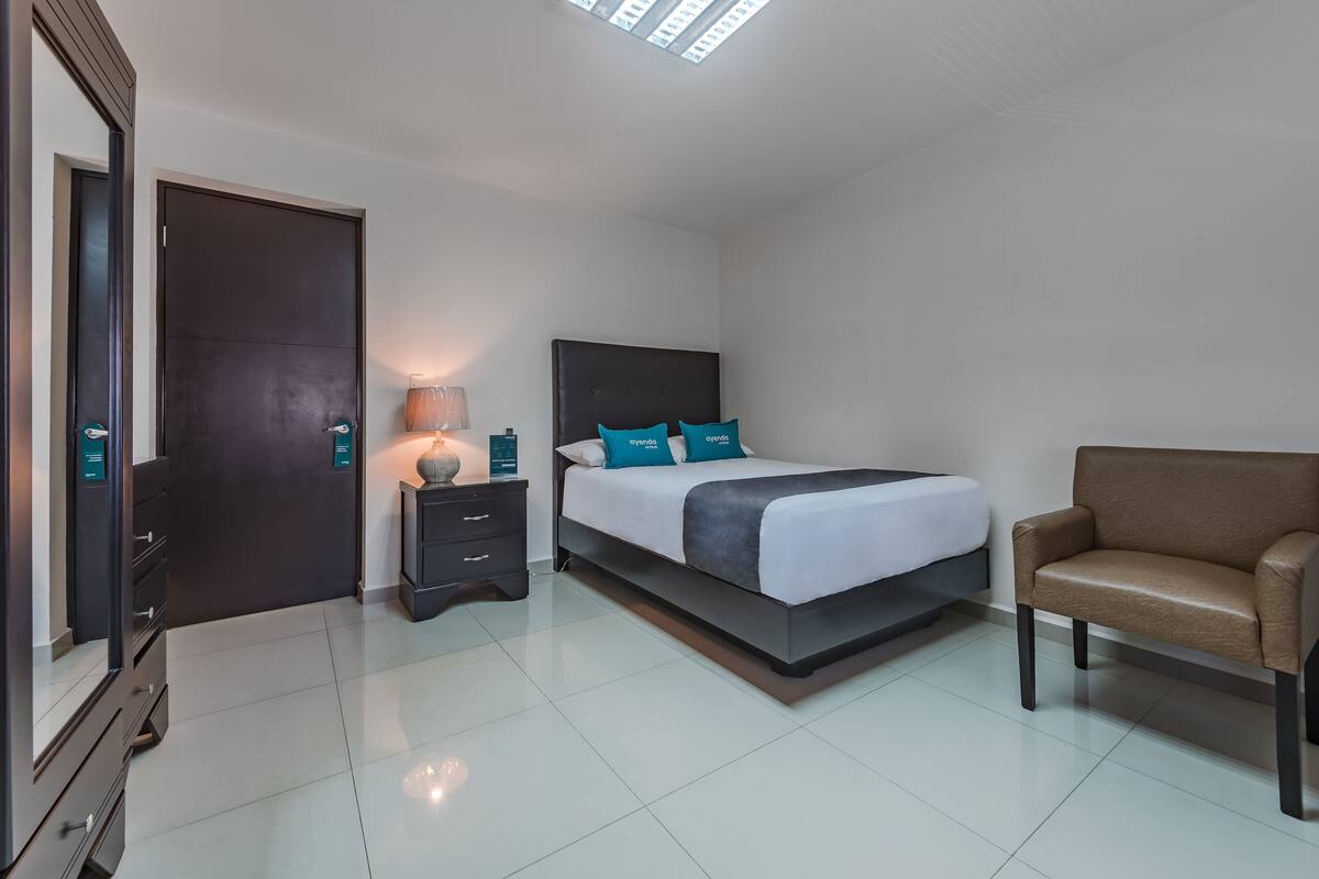 A modern hotel room with a large bed, a nightstand, a lamp, and a sofa.