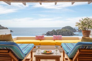 A balcony with a yellow sofa, striped cushions, a table with a plate of food and glasses, and a potted plant. -  Casitas in Careyes (Costa Careyes)