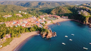 Vista aérea de un pueblo costero con playa, afloramientos rocosos y barcos en el agua.