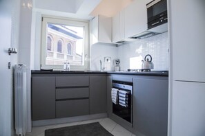 A modern kitchen with grey cabinets, a built-in oven, and a window overlooking a building.