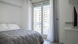 Une chambre à coucher avec un lit, une fenêtre avec des rideaux et un téléviseur à écran plat posé sur un meuble.