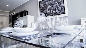 Un espace repas moderne avec une table en verre dressée pour six personnes, des assiettes blanches et des verres à vin transparents.
