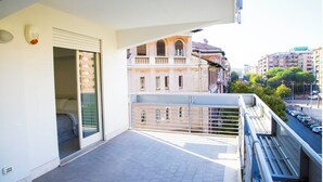Un balcon donnant sur un immeuble doté de fenêtres en arc de cercle et de balcons, avec un sol carrelé et une balustrade.