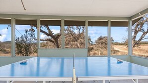 Una mesa de ping pong en un espacio cubierto con ventanas que dan a un paisaje seco.