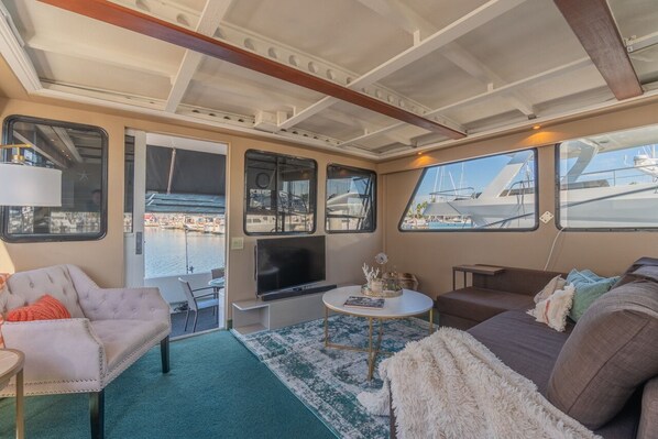 A cozy interior with a sofa, armchair, and a small table with a TV. Large windows offer views of the marina.