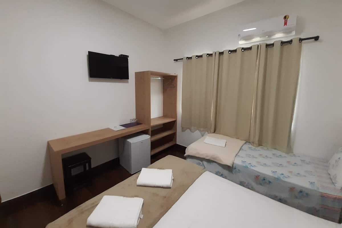 Ein Hotelzimmer mit Bett, Schreibtisch, Kleiderschrank, Spiegel und einem Fenster mit Vorhängen.