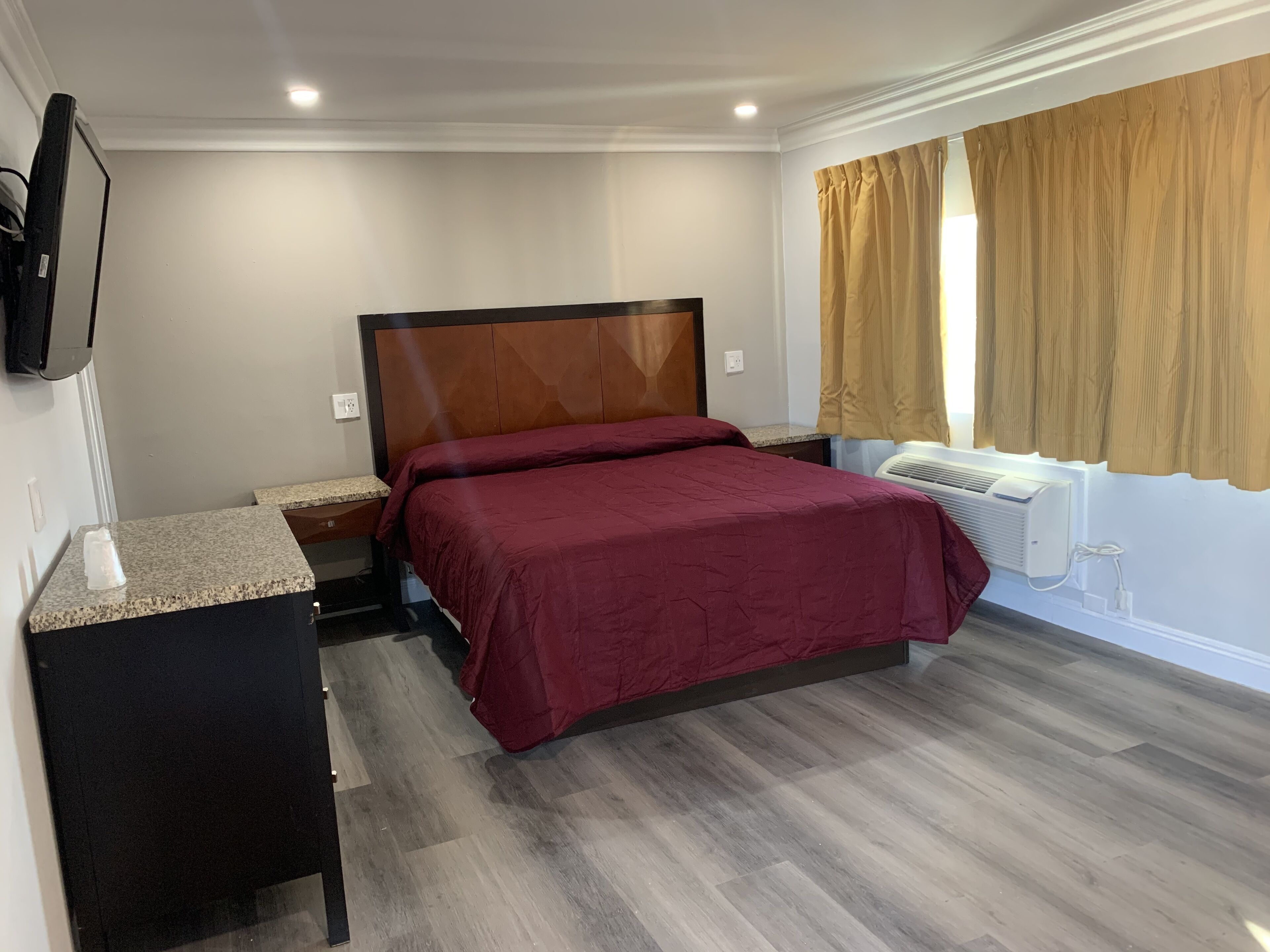 A hotel room with a bed, a nightstand, a TV mounted on the wall, and a window with curtains.