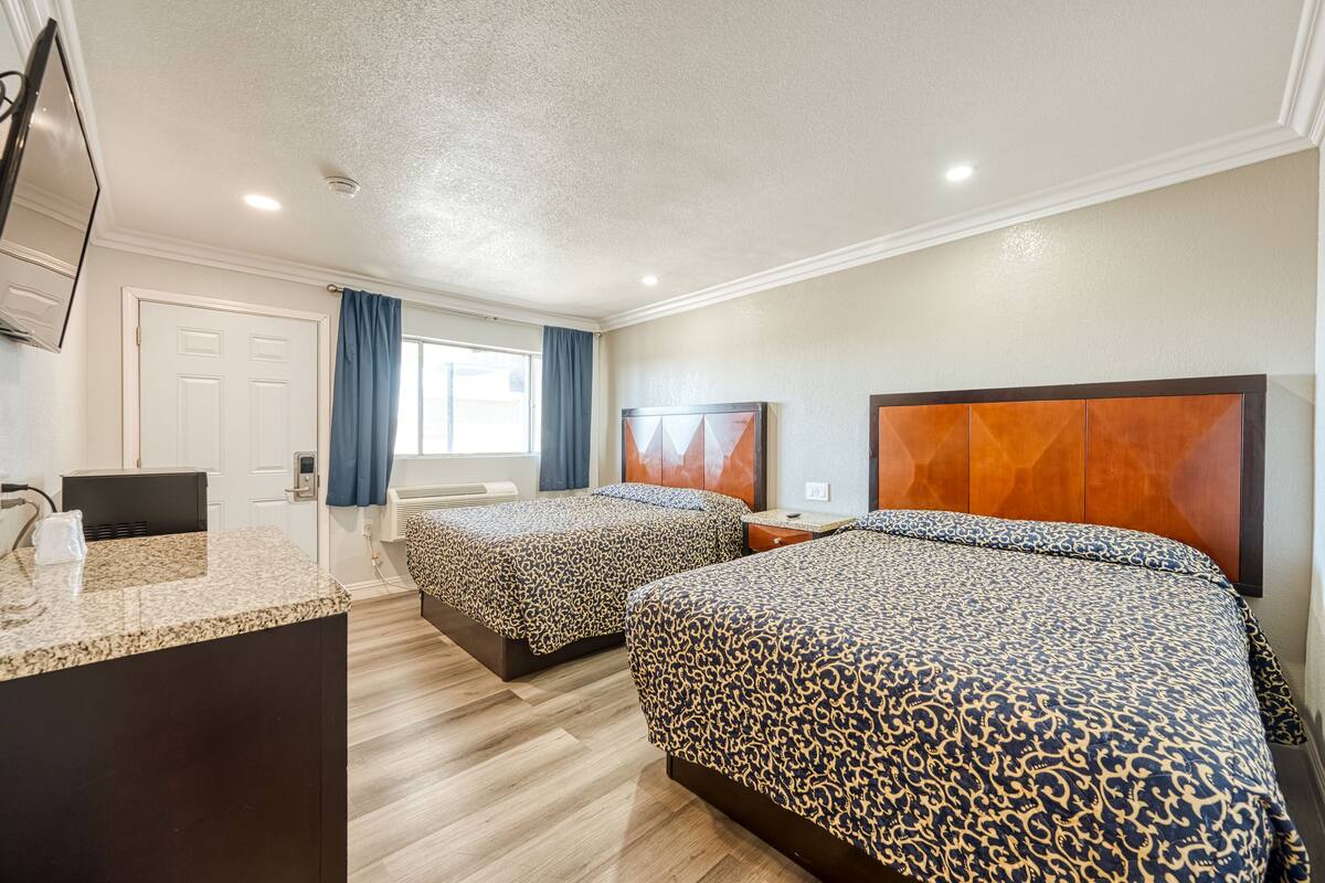 A hotel room with two beds, a desk, a TV, and a bathroom.
