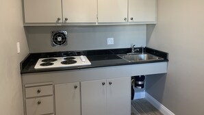 A kitchen with white cabinets, a black countertop, a stainless steel sink, and a stove with four burners. - ERTH INN by AGA - Mojave (Mojave)