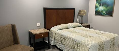 A bedroom with a bed, a chair, a nightstand, and a lamp.